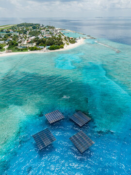 Aerial view of SolarSea floating solar power plant by Swimsol on turquoise coral reef waters near the tropical island coastline at Dharavandhoo, Baa Atoll, Maldives.