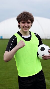 Young man football player holding soccer football ball screaming proud and celebrating victory very excited. Vertical video