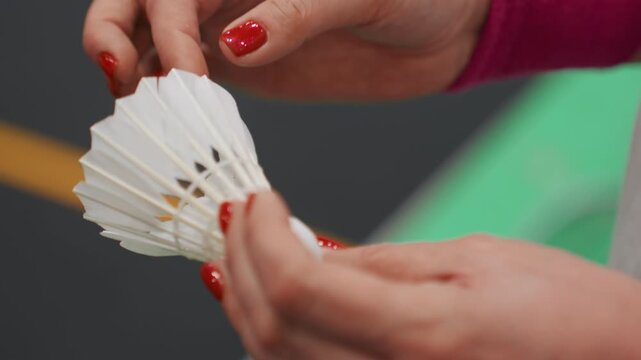 Examining shuttlecock through close inspection. Closeup view of hand inspecting badminton shuttlecock. Close and detailed look at hand scrutinizing shuttlecock on indoor court surface