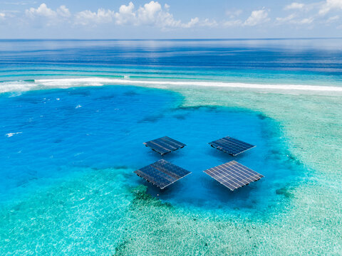 Aerial view of SolarSea floating solar power plant by Swimsol in a turquoise lagoon with coral reefs and deep blue ocean in Dharavandhoo, Baa Atoll, Maldives.