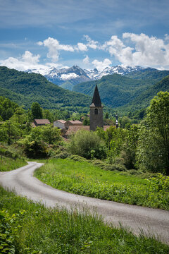 Country road to Erce mountain village in the middle of the greenery , with snow-capped peaks in the background. Ariege Pyrenees France
