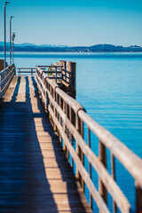 Fototapeta premium Alpine spring view with a ship pier and Fraueninsel island at Lake Chiemsee, Chieming, Chiemgau, Traunstein, Bavaria, Germany