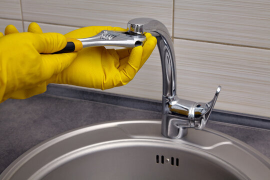 repairing a kitchen sink faucet with gloves and a wrench