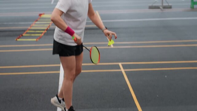 White woman practicing badminton ladder drills, footwork session combining agility ladder and shuttle placement, fitness trainee working on speed and coordination, indoor court lines visible, pink