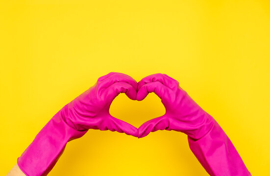 Hands in pink gloves making heart shape on yellow
