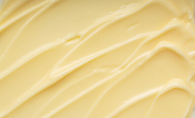Abstract background of creamy yellow texture with smooth ripples and swirls, thick custard or cosmetic cream close-up