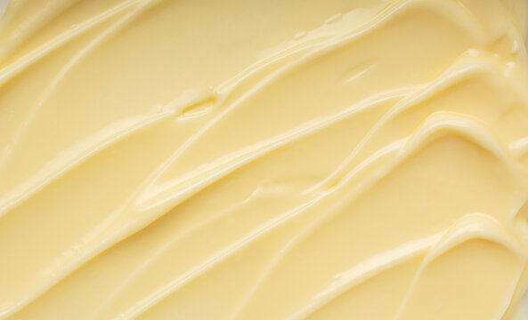 Abstract background of creamy yellow texture with smooth ripples and swirls, thick custard or cosmetic cream close-up