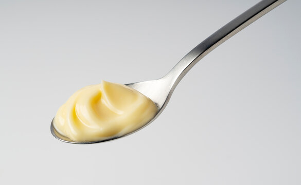 Creamy mayonnaise with elegant swirl on a stainless steel spoon, thick yellow sauce condiment on light gray background