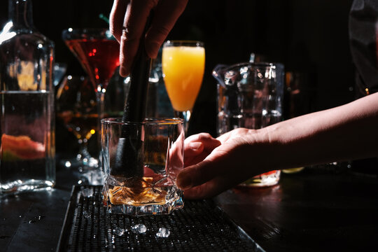 Bartender woman using muddler to crush ingredients in crystal glass. Professional technique of mashing fruit and herbs for cocktail base.