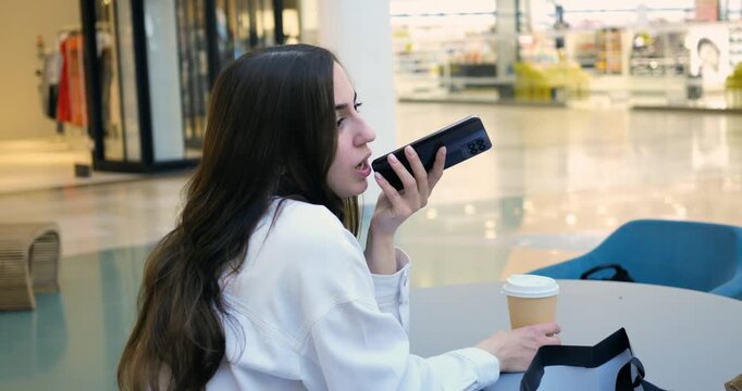 Female using phone loudly. Female individual engaging in loud conversation at shopping mall. Woman with mobile phone loudly communicating while seated with shopping bags in busy mall setting