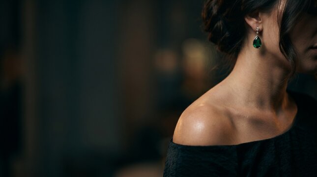 Elegant woman wearing a green emerald teardrop earring in a dark room