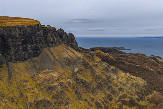 Aerial view of the dramatic rock formations and steep cliffs of The Quiraing overlooking the sea under a cloudy sky in the Isle of Skye, Scotland, United Kingdom.