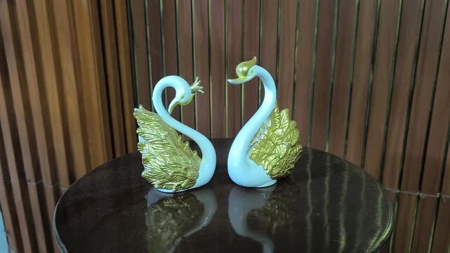 elegant white and gold swan figurines forming a heart shape on a glossy table, symbolizing love and harmony with a warm wooden background