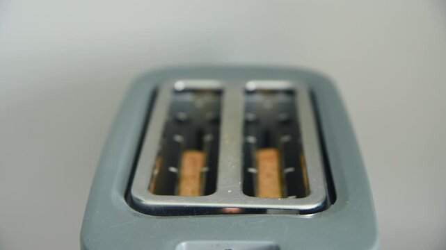 Close up of modern metallic toaster slots with bread pieces inside blurred background