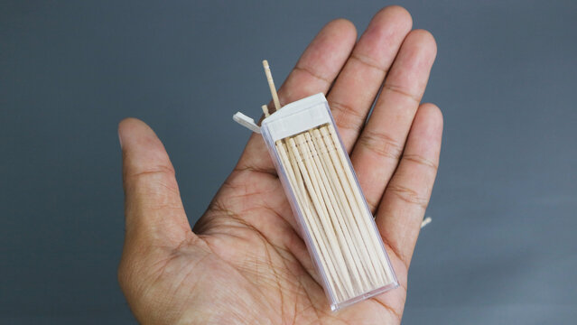 Close up hand holding small plastic box of wooden toothpicks