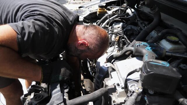 Professional repairman inspecting engine of a car at workplace. Male auto mechanic working under hood of vehicle check motor outdoor. Concept of maintenance and automobile diagnostic. Slow motion