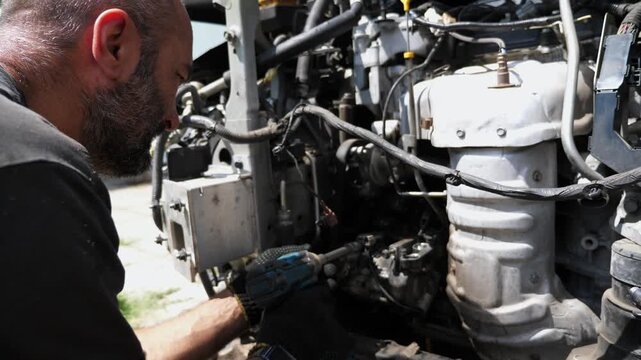 Male repairer removing bolts into car detail with electric tool at workplace. Professional mechanic repairing automobile outdoor. Auto repairman making maintenance of vehicle. Transport diagnostic