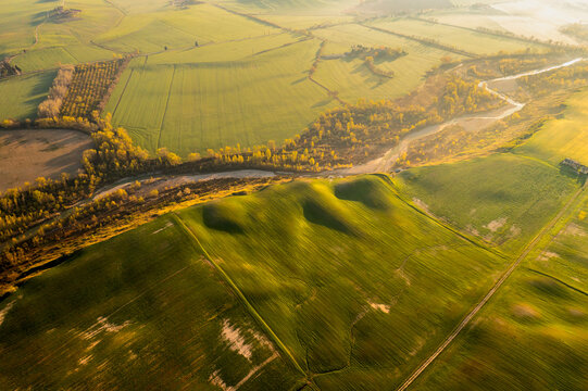 Tuscany, Italy: Aerial view of Orcia valley's rolling green fields, winding river, and golden autumn trees bathed in warm light, a serene tourism destination near Pienza.