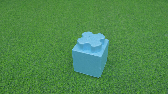 Blue foam block on grass, sensory play prop for early learning, textured soft cube, bright daylight, minimal composition with vivid lawn backdrop, singleobject focus, tactile surface inviting touch