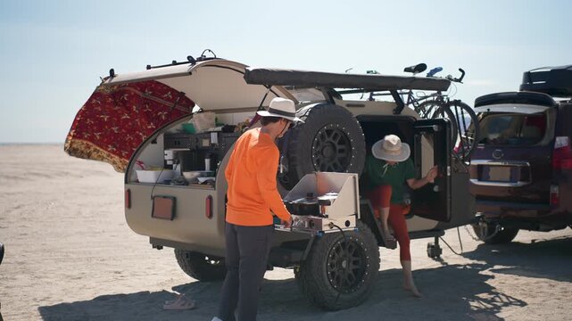 Mature man prepares a meal on a stove while camping with a teardrop camper on the beach in Baja California, Mexico.