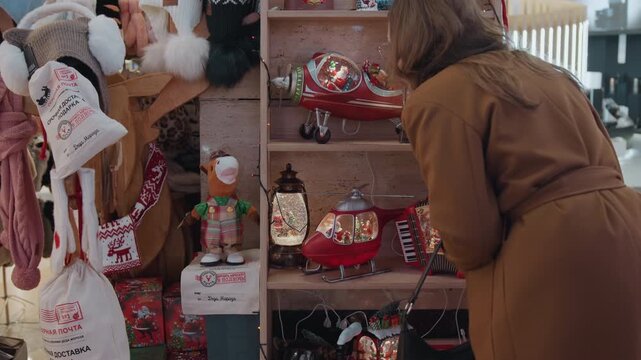 White woman browsing festive market shelf, coatclad shopper leans into display examining helicopter ornament, lanterns, nutcrackers and snow globes warm mall lighting and intimate holiday atmosphere