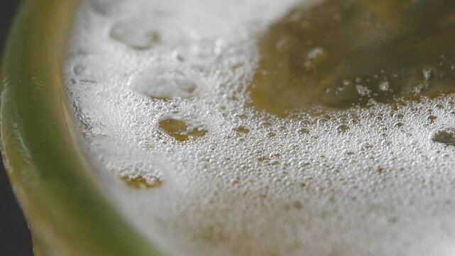 4K close-up frothy white beer foam head on golden amber beer inside a glass. 
