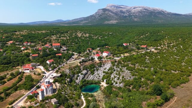 Aerial view of the Cetina River spring known as the Eye of the Earth with a church and village in the background, Dalmatian Hinterland, Croatia