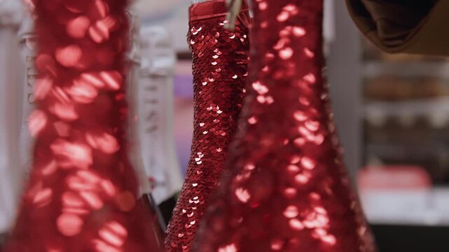 Red sequin dresses on boutique rack, closeup of shopper hand browsing glittering gowns under warm store lighting, festive holiday mood, shallow depth of field, detailed sequined texture and bokeh