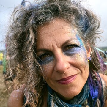 Close-up of messy, glitter-covered hair and face paint, authentic exhausted but happy expression, age-positive festival goer