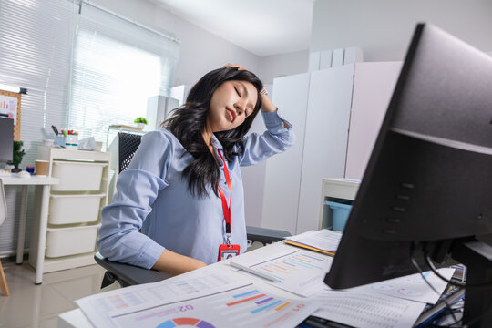 Exhausted woman office worker sitting at desk expressing intense stress with severe neck pain stretching sore muscles by business computer monitor and paperwork documents