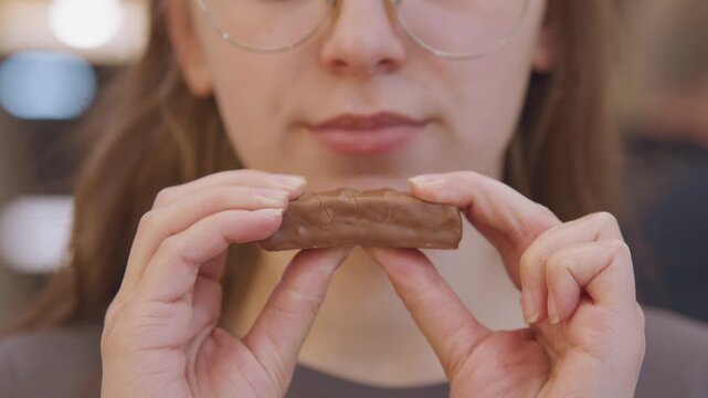 Woman examines and delicately tastes chocolate piece. Woman carefully evaluates and samples chocolate in detail. Woman meticulously inspects and gently tastes chocolate bar with focused attention