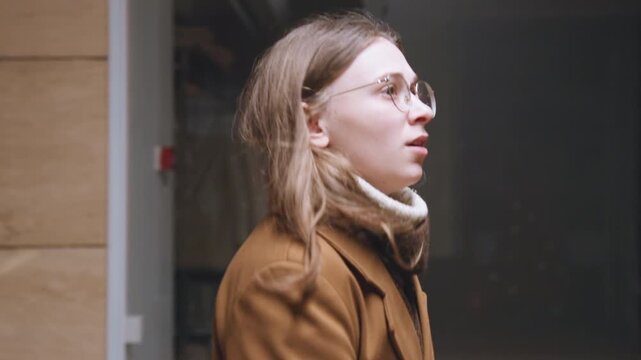Lady pauses at store with reflective glass. Evening scene featuring woman in brown coat and neon glow. Pearl illuminated mall scene with woman hesitating outside storefront with mannequins