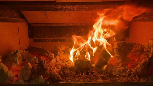 Slow motion close-up of burning logs in a fireplace with bright orange flames. Handheld shot of a wood-burning hearth, creating a warm, cozy and cinematic atmosphere. Interior winter background