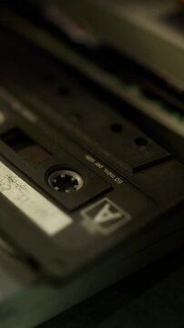 A black cassette tape with visible markings sits on a table. It is surrounded by other objects in a living room. The time shows an interest in old music recording formats.