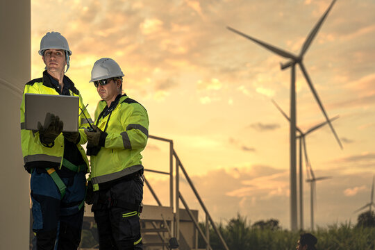 Male engineers analyzing smart grid data via laptop at onshore wind farm. Integrating advanced technology to drive the global clean energy transition.