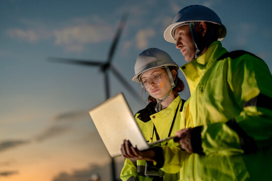 Engineers analyzing smart grid data via laptop at onshore wind farm. Integrating AI technology to drive the global clean energy transition.