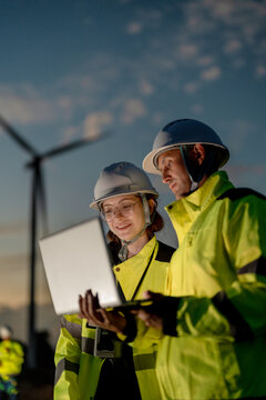 Engineers analyzing smart grid data via laptop at onshore wind farm. Integrating AI technology to drive the global clean energy transition.