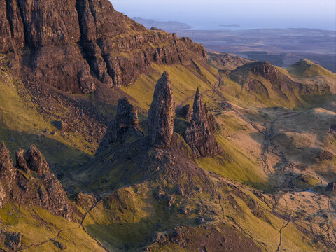 Aerial view of the Old Man of Storr rock formation with jagged pinnacles and grassy slopes during golden hour Isle of Skye, Scotland, United Kingdom.
