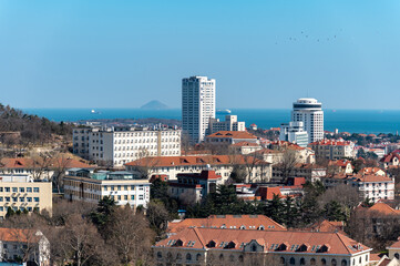 Qingdao red tile old town with white high rise apartment towers and distant blue sea and island coastal cityscape, China © 子程 龚