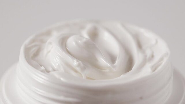 Open cosmetic jar with smooth cream texture rotating on white background showcases swirl textured moisturizing cream inside. Macro footage of spinning cosmetic container with thick, whipped cream.