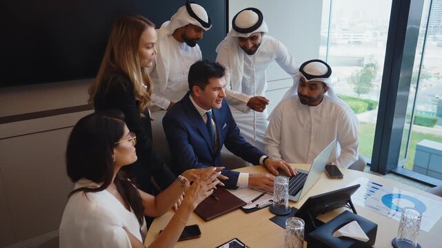 Corporate business event with emirati and western business people international business team collaborating around a conference table reviewing strategy documents and laptops