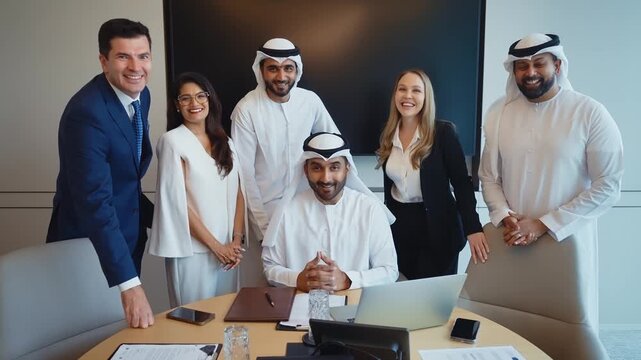 Corporate business event with emirati and western business people international business team collaborating around a conference table reviewing strategy documents and laptops