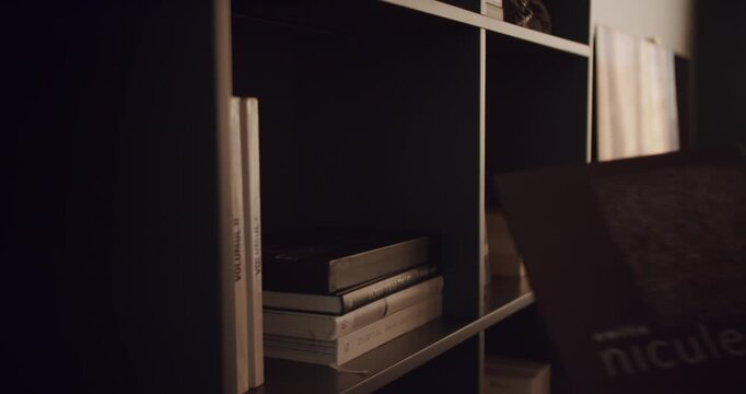 A woman's hand reaches for a book on a shelf filled with various books. The warm lighting and the quiet atmosphere create a cozy and inviting scene that embodies the joy and fulfillment of reading.