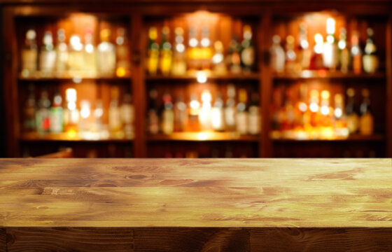a wooden tabletop in the foreground and a blurred background of a bar with shelves filled with alcoholic drinks
