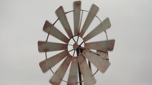 A rusty windmill spins against a stark white sky. This evokes feelings of nostalgia, resilience, and the passage of time. The scene is peaceful yet powerful, capturing the essence of rural life.
