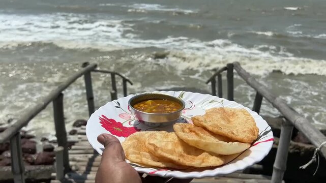 A woman holding hot, golden-brown dal puris and spicy chana masala served fresh on the shore with the beautiful crashing sea waves in the background, capturing a relaxing holiday vibe.