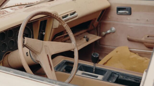 Dusty, abandoned car interior in Morocco. The steering wheel and dashboard show signs of age and decay. The seats are torn. This evokes a sense of nostalgia, history, and forgotten journeys.