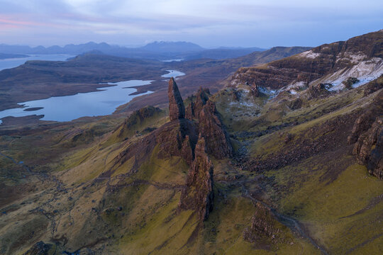 Aerial view of The Storr rock formation with its iconic jagged pinnacles overlooking the calm waters of Loch Leathan under a soft morning sky in Isle of Skye, Scotland, United Kingdom.