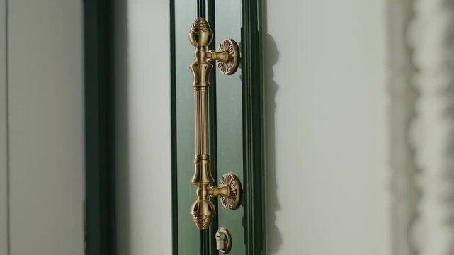 Close-up of a gold ornate door handle on a stylish dark, emerald green wooden door with intricate details. The shot offers a sense of luxury, sophistication, and old-world charm.