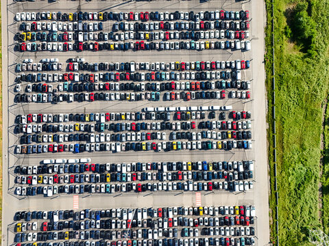 Aerial view of rows of colorful cars parked in a large logistics lot next to green fields in Rivalta di Torino, Piedmont, Italy.